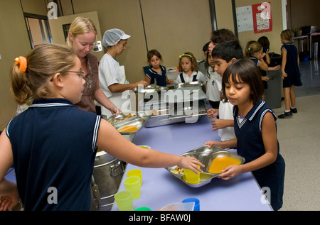 Busy junior school canteen with girl pupil helping the lunch time staff serving healthy balanced meals Stock Photo