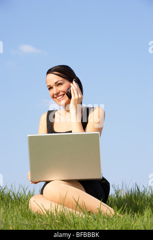 Woman Using Laptop And Mobile Phone Outdoors In Countryside Stock Photo
