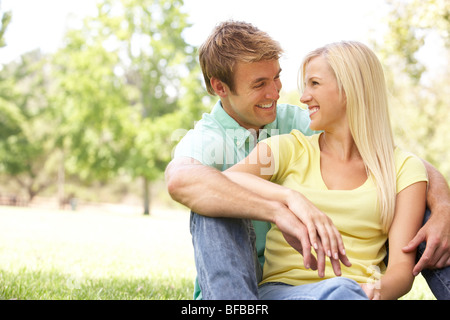 Portrait Of Young Couple Sitting In Park Stock Photo