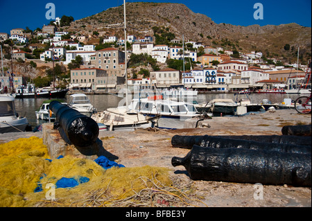 Cannons, yellow fishing nets and boats in the harbor of Hydra island, Greece Stock Photo