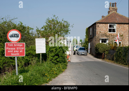 Car driver paying at Aldwark toll bridge, handing money to man on duty by booth. (Clear signage & toll keeper's house) - North Yorkshire, England, UK. Stock Photo