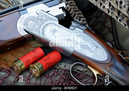 Finely engraved side plate of 12 bore over and under shotgun with two red cartridges on game bag with pheasant feathers Stock Photo