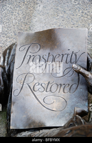 Close-up of a bronze statue showing a man holding a piece of paper with the words ' Prosperity Restored ' written on it. Stock Photo