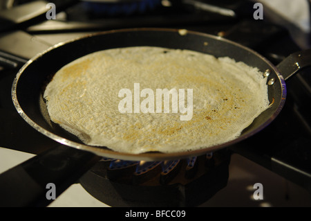 A frying pan on a gas fueled hob with a pancake cooking in it. Stock Photo