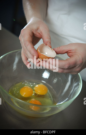 A female caterer holds a broken egg shell in her hands over a clear glass bowl after emptying the yokes into it.