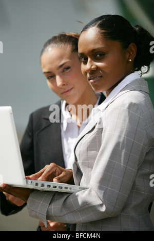 Two young women with laptop facing camera Stock Photo