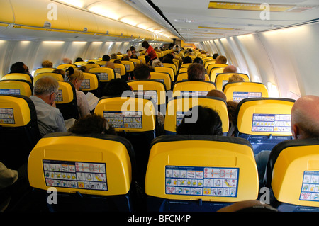 seats and seated passengers during a flight in a Ryanair aircraft viewed from the backshowing emergency proceedure notice Stock Photo