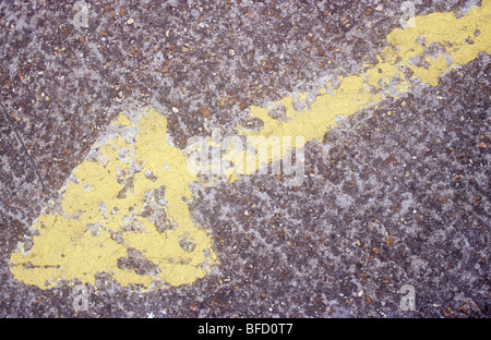 Large yellow arrow painted on rough concrete surface but largely worn away through use Stock Photo