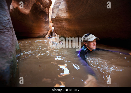 A woman swims through a winding corridor filled with water in a slot canyon in Utah. Stock Photo