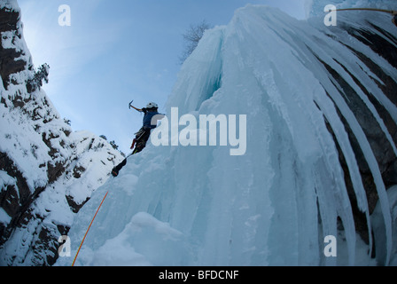 View from below of a professional female climber ice climbing a frozen waterfall in Colorado. Stock Photo