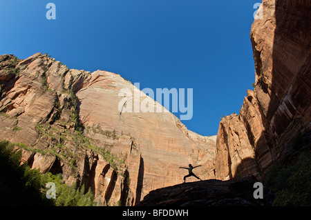 A young woman practicing yoga on a rock is silhouetted against distant cliffs. Stock Photo