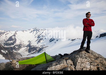 A young climber stands on a rock outcrop near his tent while climbing on a glacier in the mountains.