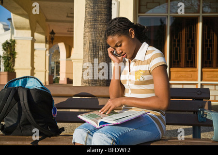 African American teen girl 13-15 year old talking on mobile phone while doing homework. California  United States  MR Stock Photo