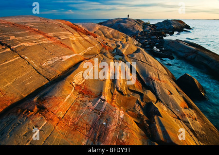 Man in the background on pre-cambrian shield at sunset on Georgian Bay, south of Philip Edward Island, Ontario, Canada Stock Photo