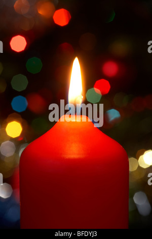 red christmas candle burning alight in front of a christmas tree Stock Photo