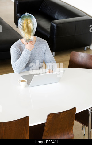 Man holding a lit lightbulb in front of his face and using a laptop computer, Montreal, Canada Stock Photo
