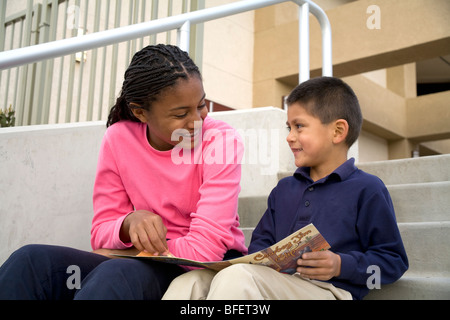 Older teenage girl reads a book talks smiling smiles encouraging encouragement boy 5-6 years old United States MR © Myrleen Pearson Stock Photo