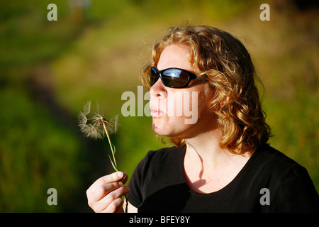 Woman blowing the seeds of the Western salsify or goatsbeard in a meadow (Tragopogon dubius), on a warm afternoon. Stock Photo