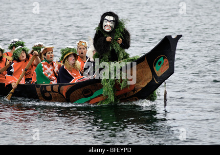 Native man standing at bow of canoe with white mask during Tribal Journeys event at North American Indigenous Games in Duncan. Stock Photo