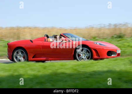 Low angle profile (side view) of a Red Ferrari 360 Spider supercar in motion on the public roads driving fast Stock Photo