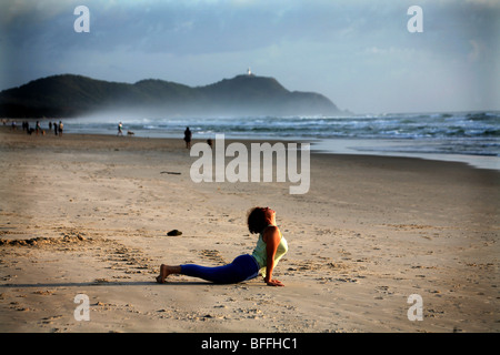A woman arches her back in the Cobra pose during a morning yoga program at Tallow beach Stock Photo