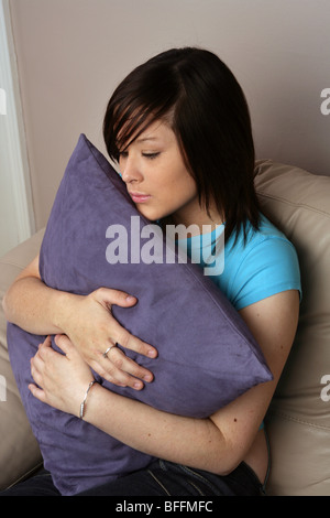Young woman sitting on sofa hugging a big cushion Stock Photo