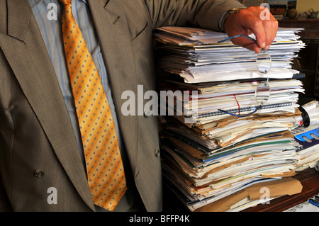 Businessman leaning on a stack of paperwork, overworked office worker or manager with pile of documents Stock Photo