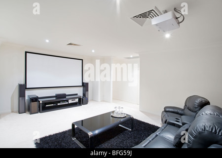 home theater room with black leather recliner chairs, projector in ceiling and projector screen on wall. Stock Photo