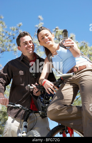 Couple on Mountain Bikes using mobile phone, photographing selves, low angle view. Stock Photo