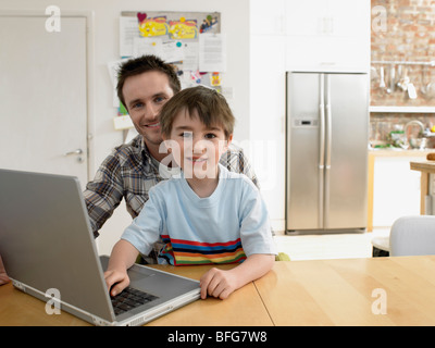 Boy (3-6) using laptop with father in kitchen, (portrait) Stock Photo