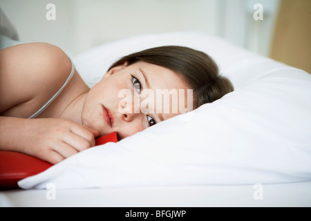 Little girl with cold in bed holding hot water bottle, portrait, close up Stock Photo