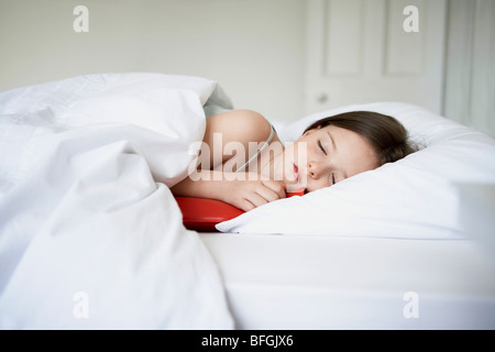 Little girl with cold in bed holding hot water bottle Stock Photo