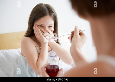 Mother giving cough syrup to reluctant daughter in bedroom Stock Photo