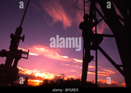 Oil industry worker climbing pump jack in Alberta, Canada, at sunset. Stock Photo