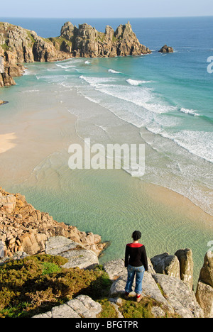 Woman standing on a rock, looking down at Porthcurno beach, Cornwall, UK Stock Photo