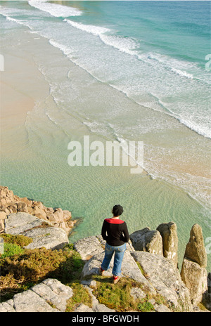 Woman standing on a rock, looking down at waves, Cornwall, UK Stock Photo