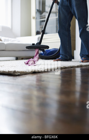 Man vacuuming tie from rug, low section Stock Photo