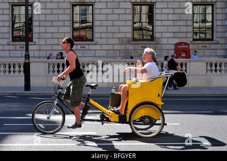 London rickshaw & driver pedalling a couple of passengers along tour of Whitehall passing government buildings sunny warm June summer day England UK Stock Photo