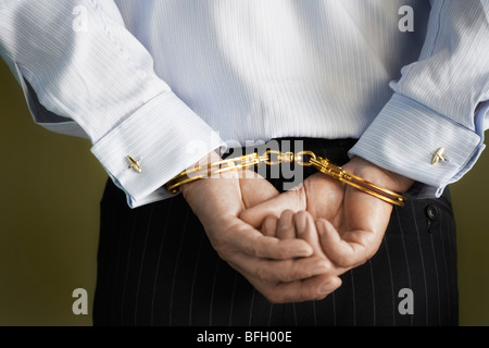 Businessman standing with hands handcuffed behind back, mid section, back view Stock Photo