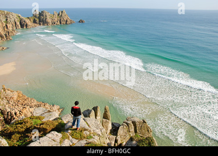 Woman standing on a rock, looking down at Porthcurno beach, Cornwall, UK Stock Photo