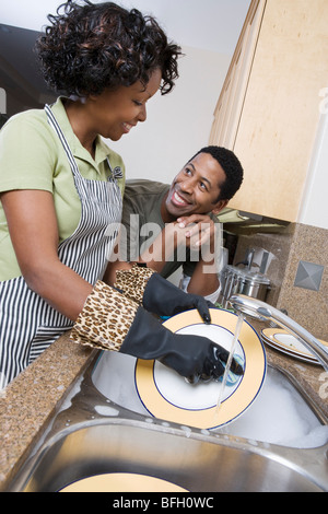 Mid-adult woman washing dishes, her boyfriend leaning on kitchen counter, looking in eyes Stock Photo