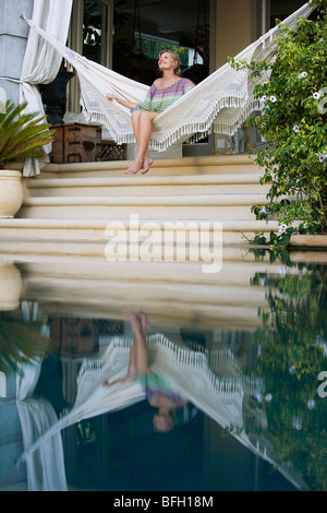 Young woman sitting on hammock overlooking swimming pool, portrait Stock Photo