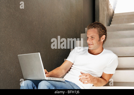 Young man sitting on stairs using laptop, portrait Stock Photo
