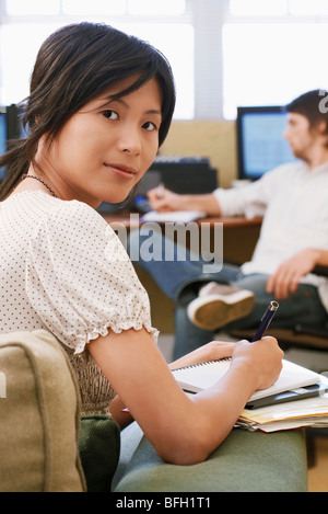 Woman Taking notes, man using computer in background. Stock Photo
