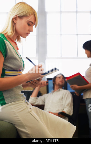 Woman taking notes with man and woman talking in background. Stock Photo