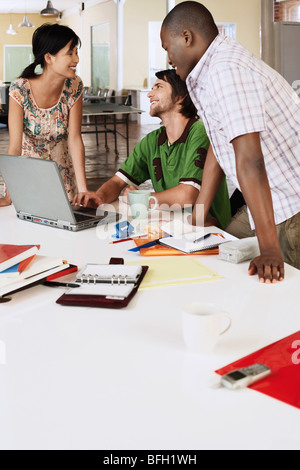 Three office workers around laptop, smiling. Stock Photo
