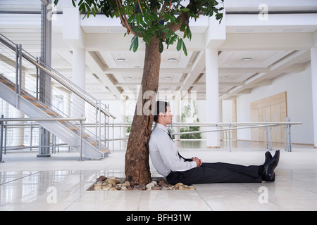Businessman resting under tree outside office Stock Photo