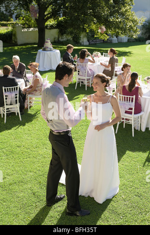 Mid adult bride and groom in garden, toasting among wedding guests Stock Photo