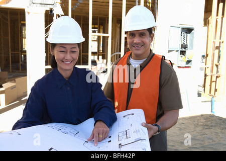 Architect and construction worker looking at blueprints on construction site Stock Photo