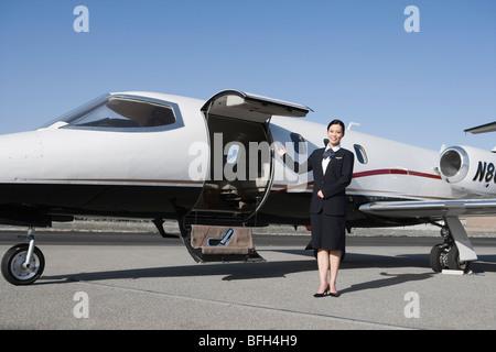 Female flight attendant standing in front of private jet on runway. Stock Photo